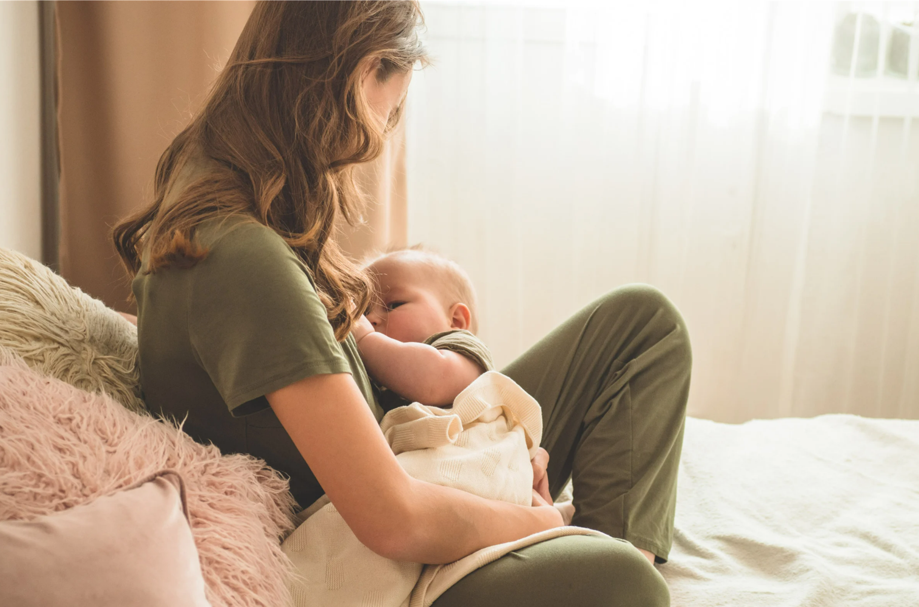 Mother nursing her baby while sitting on a bed