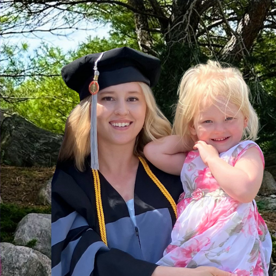 Mother wearing graduation gown and holding young daughter