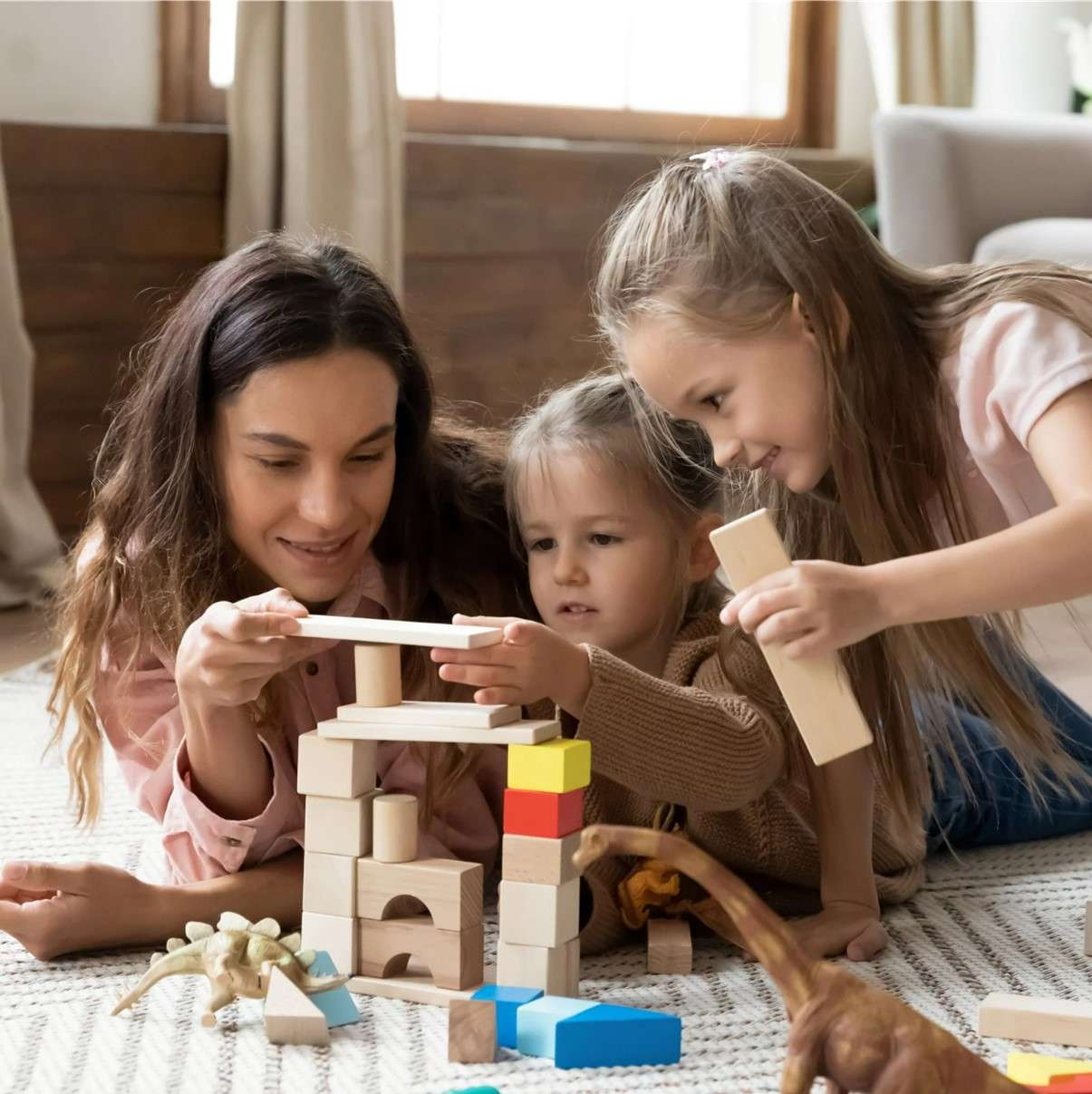 Babysitter and young girls laying on the floor and building with wooden blocks
